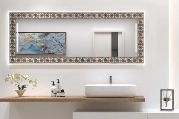 Full length backlit mirror with a unique mosaic frame above a countertop basin and white flowers.