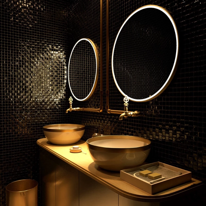 Two gold sinks with a gold frame and lighted mirrors on a black mosaic tiled wall.