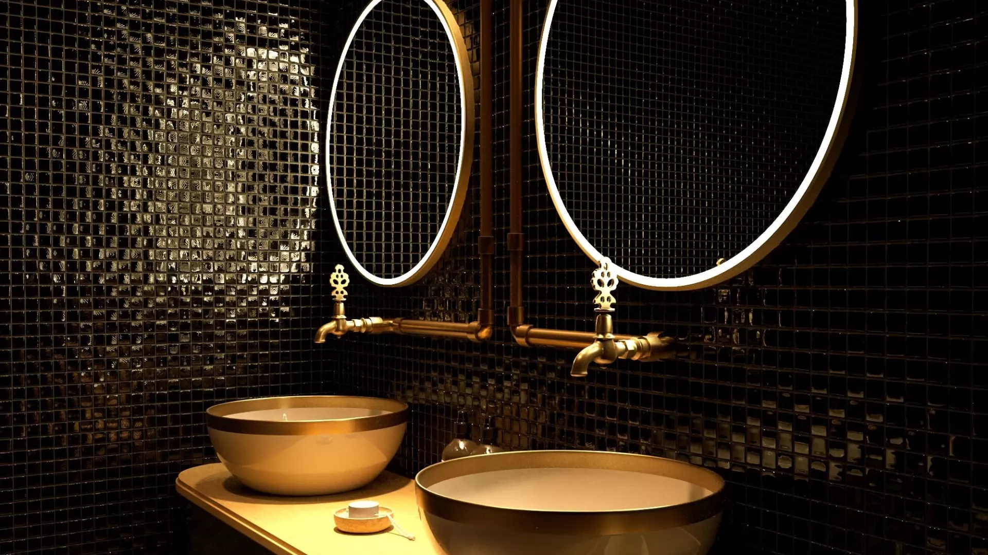 Two gold sinks with a gold frame and lighted mirrors on a black mosaic tiled wall.