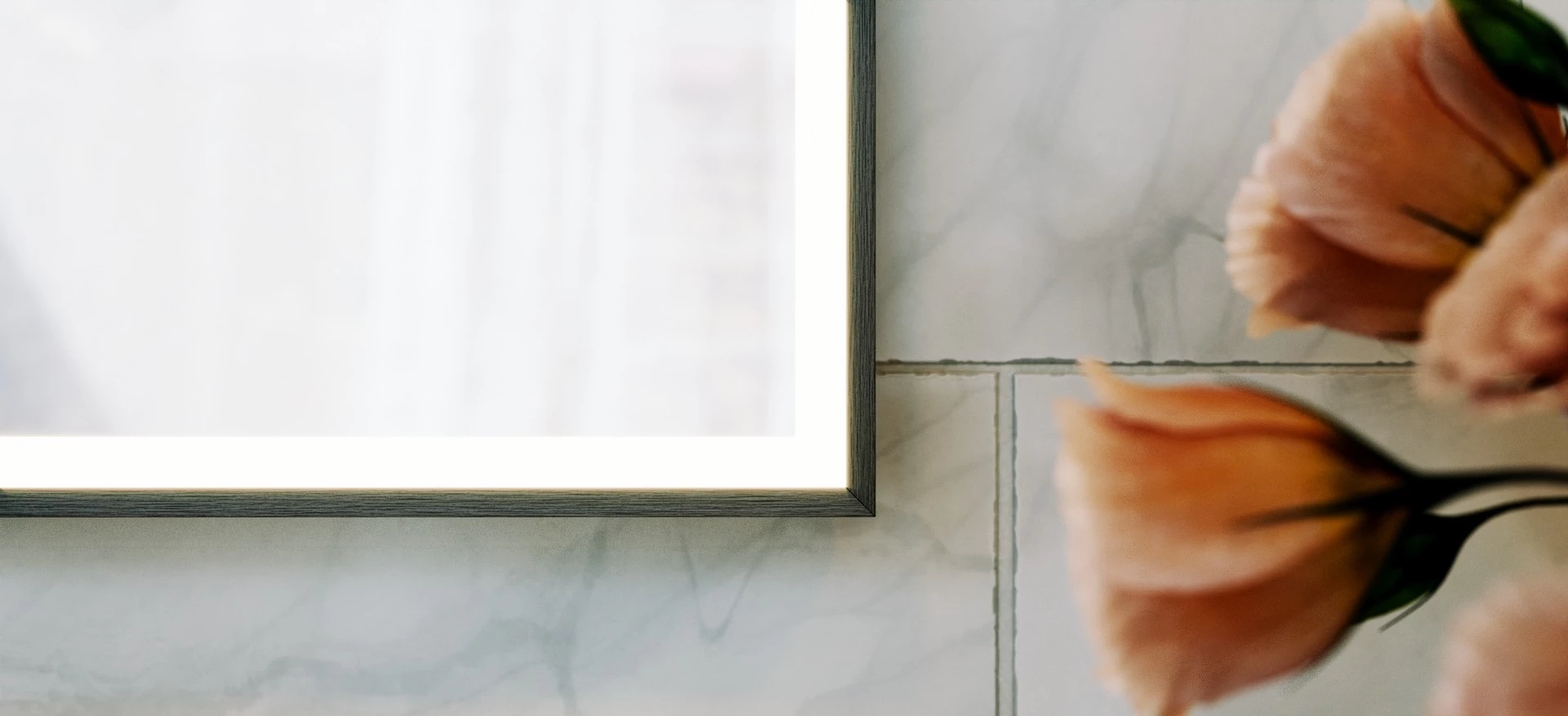 A cropped square-shaped lighted mirror with a rose flower on the side.